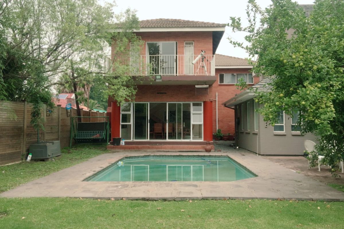 Rear view of a two-story brick house featuring a swimming pool, patio area, and a balcony accessible from the upper level.
