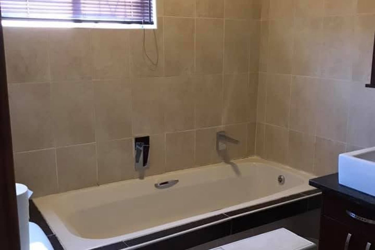 A functional bathroom featuring a built-in bathtub with wall-mounted chrome fixtures, tiled walls, and a vanity cabinet with a basin.