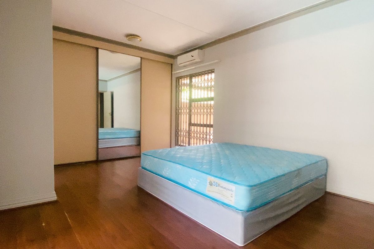 A spacious bedroom featuring laminate flooring, built-in mirrored cupboards, and an air conditioning unit, providing a clean and functional living space.