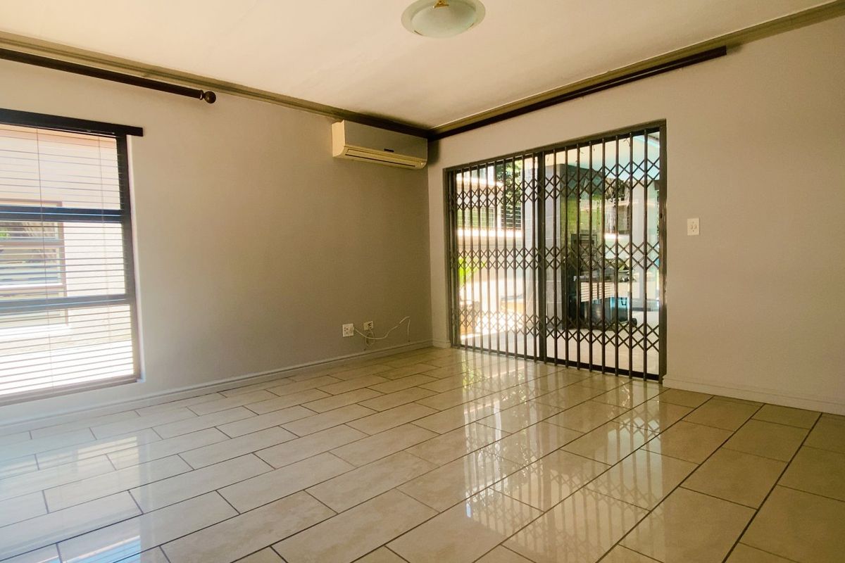 An empty living room featuring tiled flooring, a wall-mounted air conditioning unit, and a sliding glass door with a security gate leading outdoors.