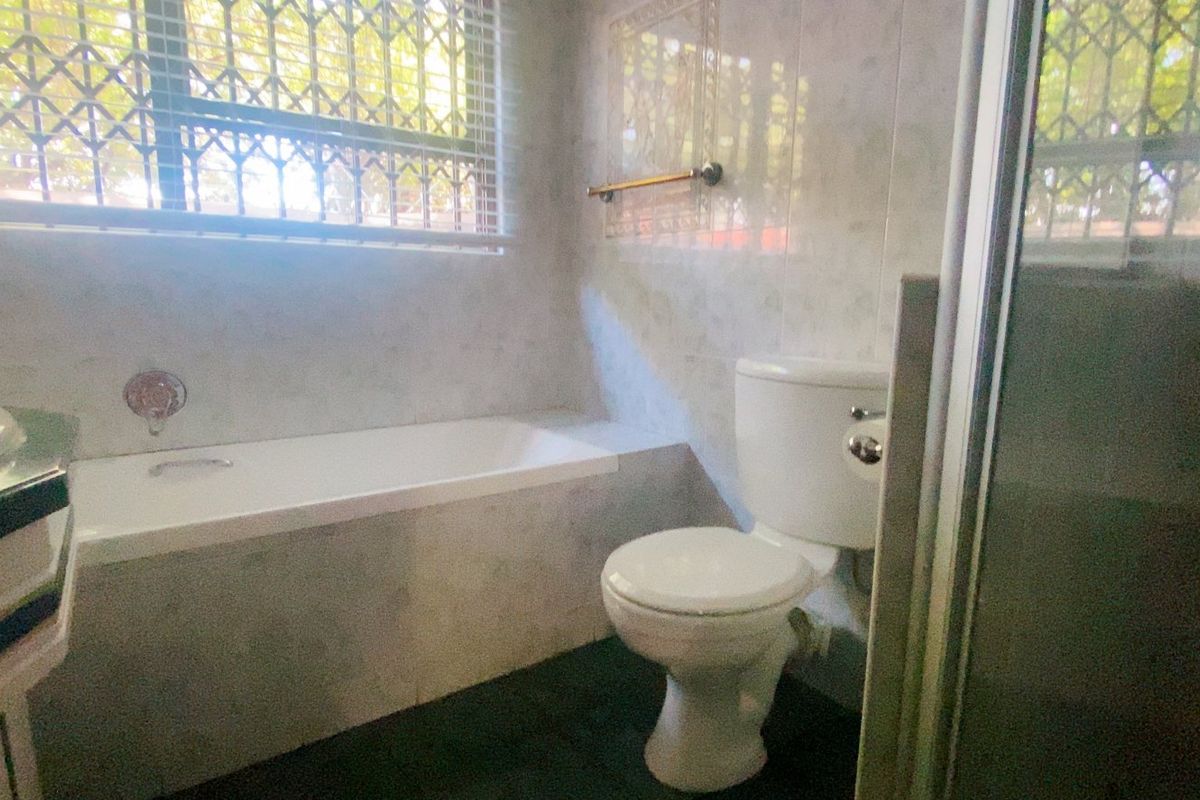 A functional bathroom featuring a built-in bathtub, toilet, and tiled finishes, equipped with a security gate on the window for added safety.