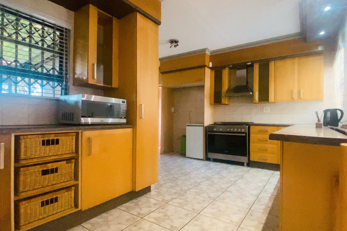 A functional kitchen featuring wooden cabinetry, tiled flooring, and a built-in extractor fan, offering a practical layout with potential for modern updates.