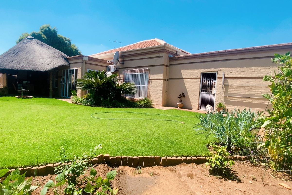 Rear view of the townhouse featuring a well-maintained lawn, a thatched lapa entertainment area, and secure access points with security gates and bars.