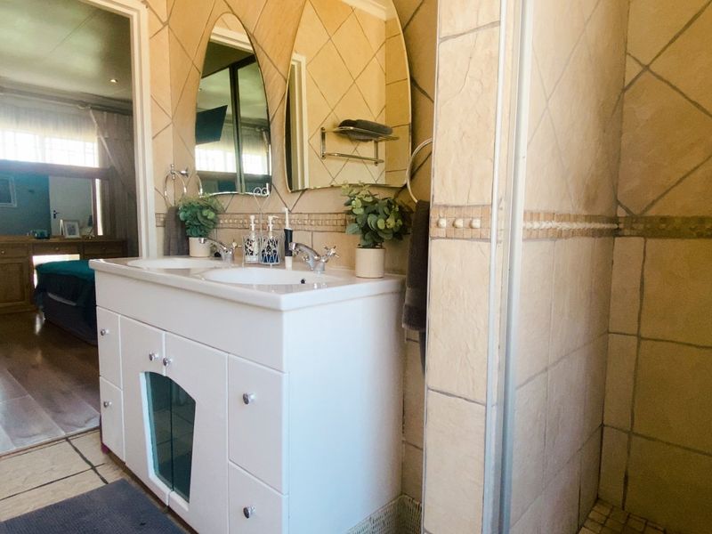 A functional bathroom featuring a double vanity, tiled walls and flooring, a shower enclosure, and a bathtub, with direct access to the adjacent bedroom.