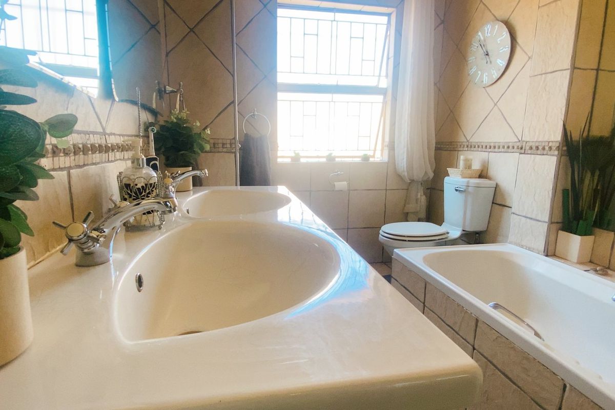 A functional bathroom featuring a double vanity, built-in bathtub, and toilet, finished with neutral wall tiling and natural light from the window.