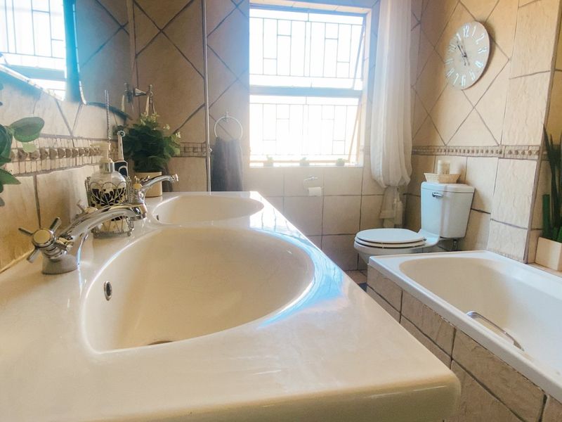 A functional bathroom featuring a double vanity, built-in bathtub, and toilet, finished with neutral wall tiling and natural light from the window.