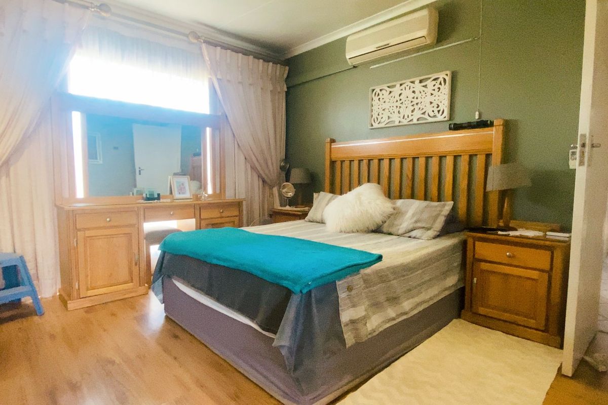 A spacious bedroom featuring laminate flooring, a wall-mounted air conditioning unit, and built-in vanity with integrated lighting.