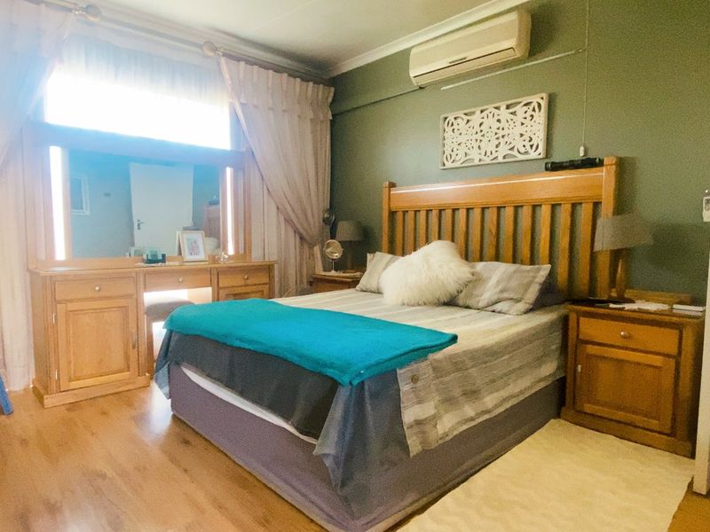 A spacious bedroom featuring laminate flooring, a wall-mounted air conditioning unit, and built-in vanity with integrated lighting.
