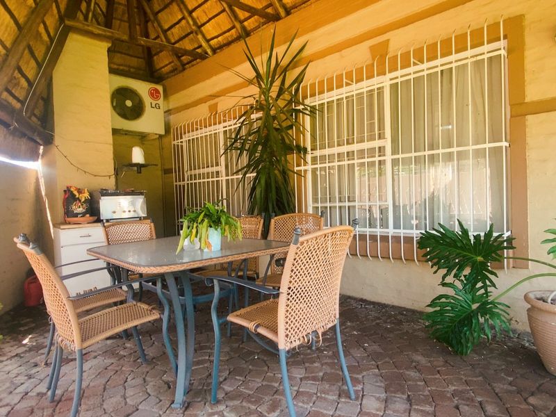 Covered patio area featuring a traditional thatch roof, brick paved flooring, and security bars on windows, providing a functional outdoor entertainment space.
