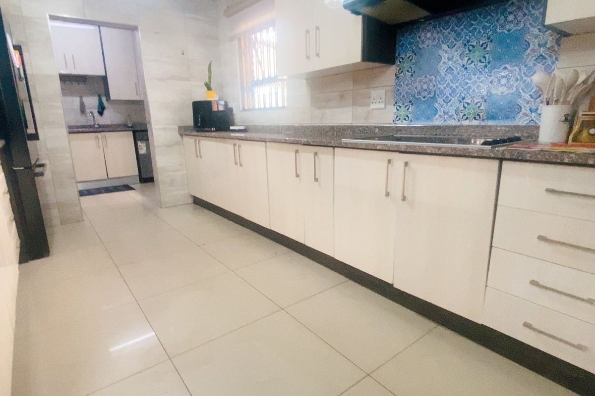 A functional kitchen featuring built-in cabinetry, stone countertops, a hob with extractor fan, and a decorative tiled splashback, with an adjacent scullery area.
