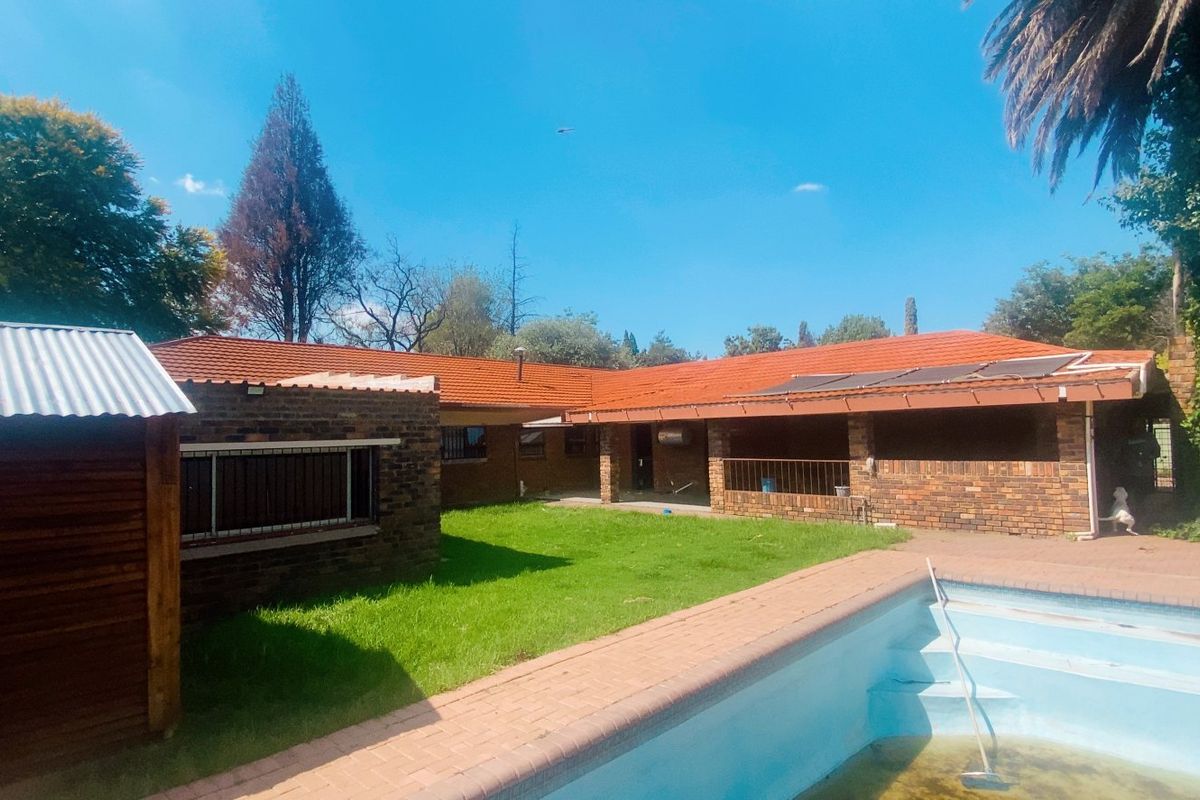 Rear view of the property featuring a brick facade, tiled roof with solar panels, a covered patio, and a swimming pool set in a garden.