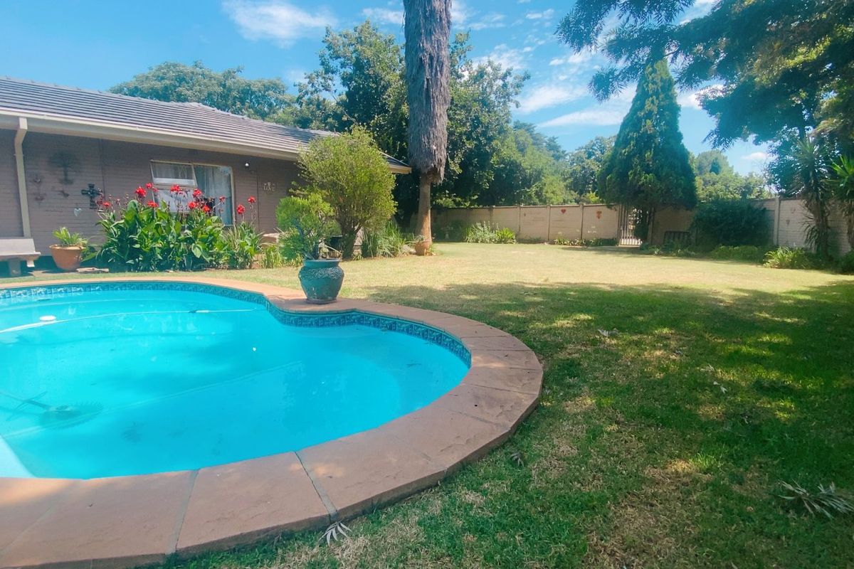 A spacious backyard featuring a swimming pool with tiled coping, a well-maintained lawn, and a secure perimeter boundary wall.
