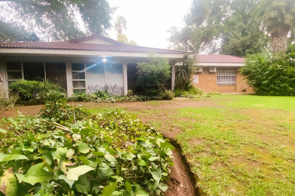 Rear view of a single-story brick residence featuring a tiled roof, security bars on windows, and an expansive garden area.