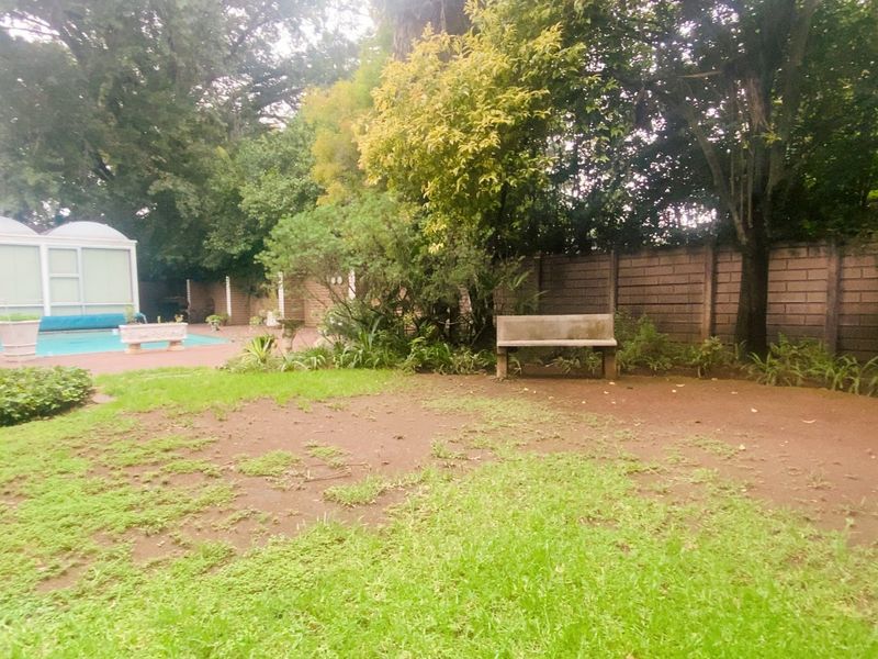 A private rear garden featuring a swimming pool, paved patio area, and established perimeter boundary walls with mature trees.