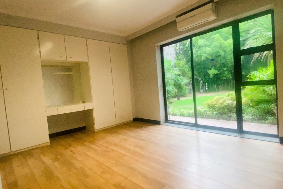 Spacious bedroom featuring built-in cupboards, a integrated desk, laminate flooring, and large sliding glass doors providing direct access to the garden.