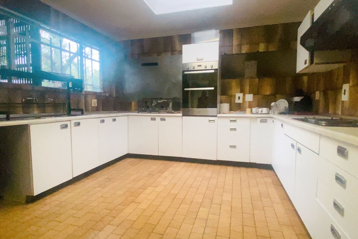 A dated kitchen featuring white cabinetry, built-in oven, hob, extractor fan, and a skylight, offering significant potential for a modern renovation.
