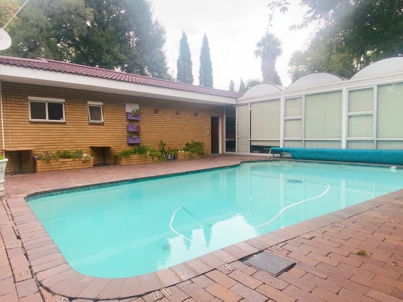 Outdoor pool area featuring a swimming pool with a cover, surrounded by brick paving and a brick-clad residential building.