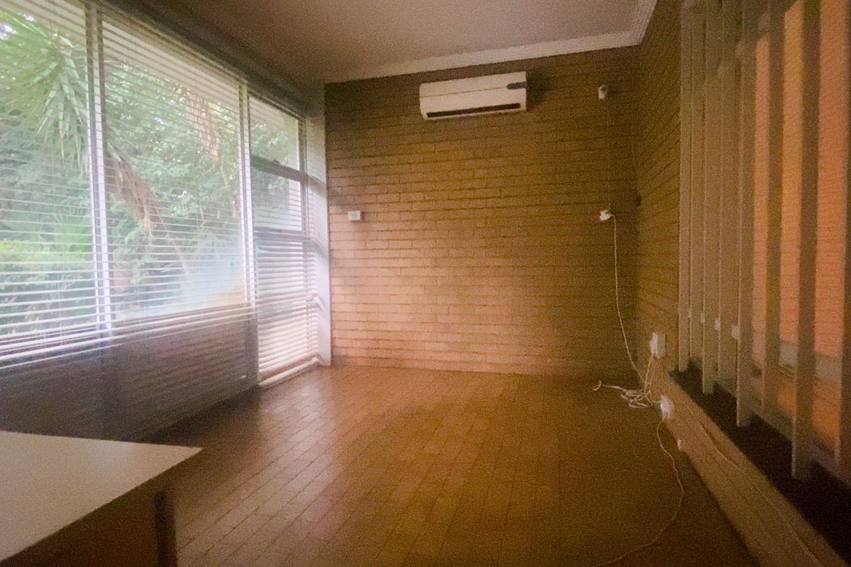 A bright, empty living space featuring timber flooring, a textured brick wall, and a split system air conditioner, with large windows overlooking the garden.