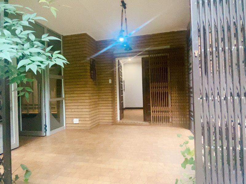 A covered entrance area featuring brick wall finishes, tiled flooring, and a secure metal gate, providing a functional and protected transition into the home.