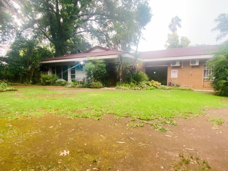 A rear view of the house featuring a brick facade, tiled roof, and established garden with lawn and mature trees.