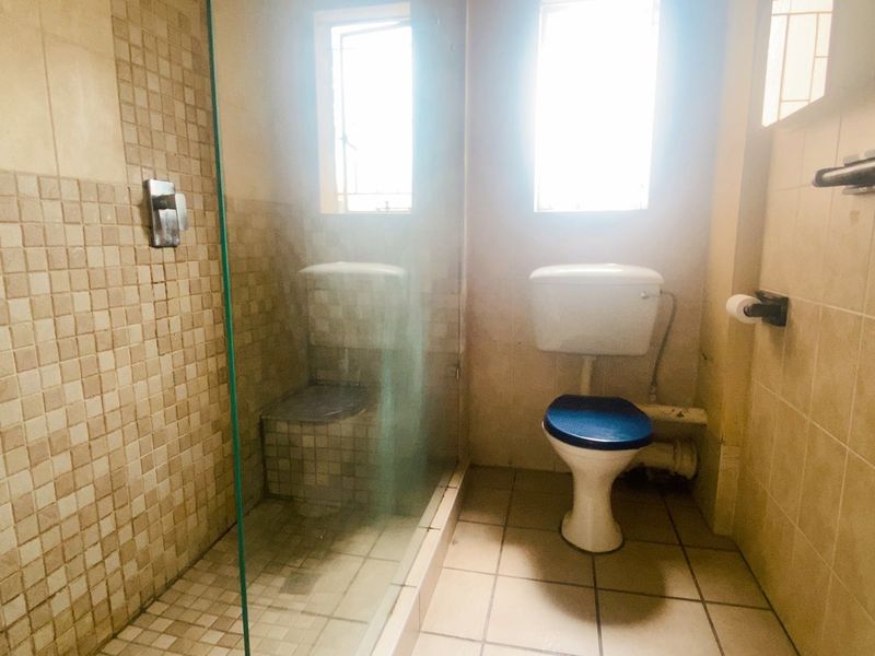 A compact bathroom featuring a glass-enclosed shower with mosaic tiling, a standard toilet, and neutral wall tiles.