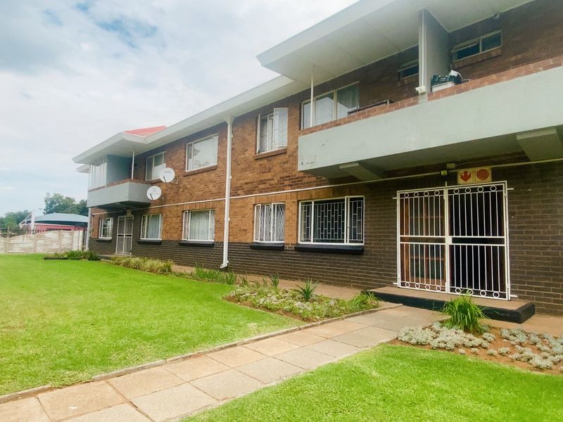 Exterior view of a multi-story apartment building featuring brick facade, private balconies, security gates, and a well-maintained communal lawn area.