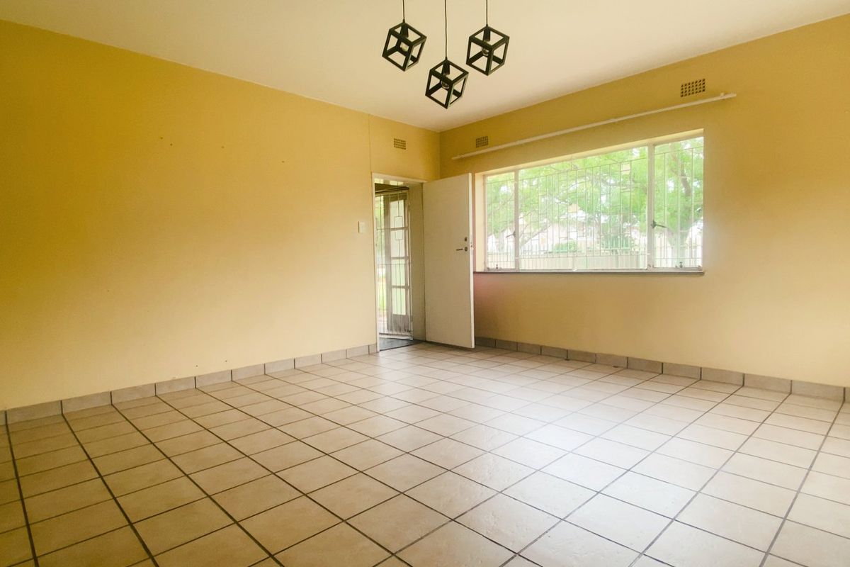 A spacious, empty living room featuring neutral tiled flooring, large windows with security bars, and a neutral color palette, ready for personalization.