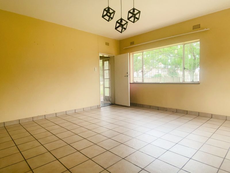A spacious, empty living room featuring neutral tiled flooring, large windows with security bars, and a neutral color palette, ready for personalization.