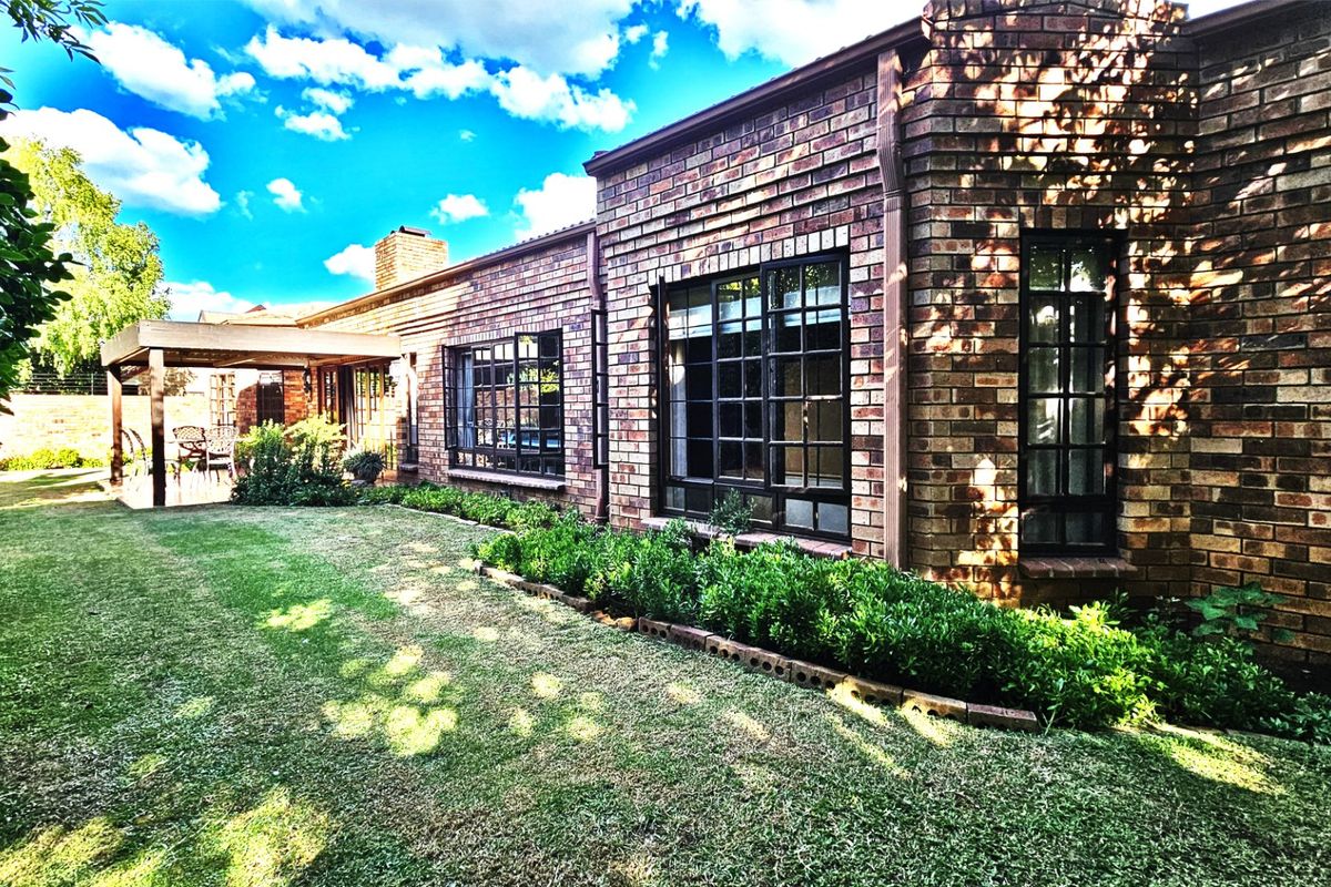 A well-maintained rear exterior view of the townhouse featuring classic brickwork, large steel-framed windows, and a covered patio overlooking a landscaped garden.
