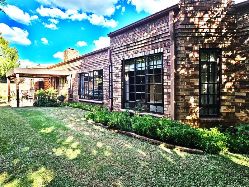 A well-maintained rear exterior view of the townhouse featuring classic brickwork, large steel-framed windows, and a covered patio overlooking a landscaped garden.