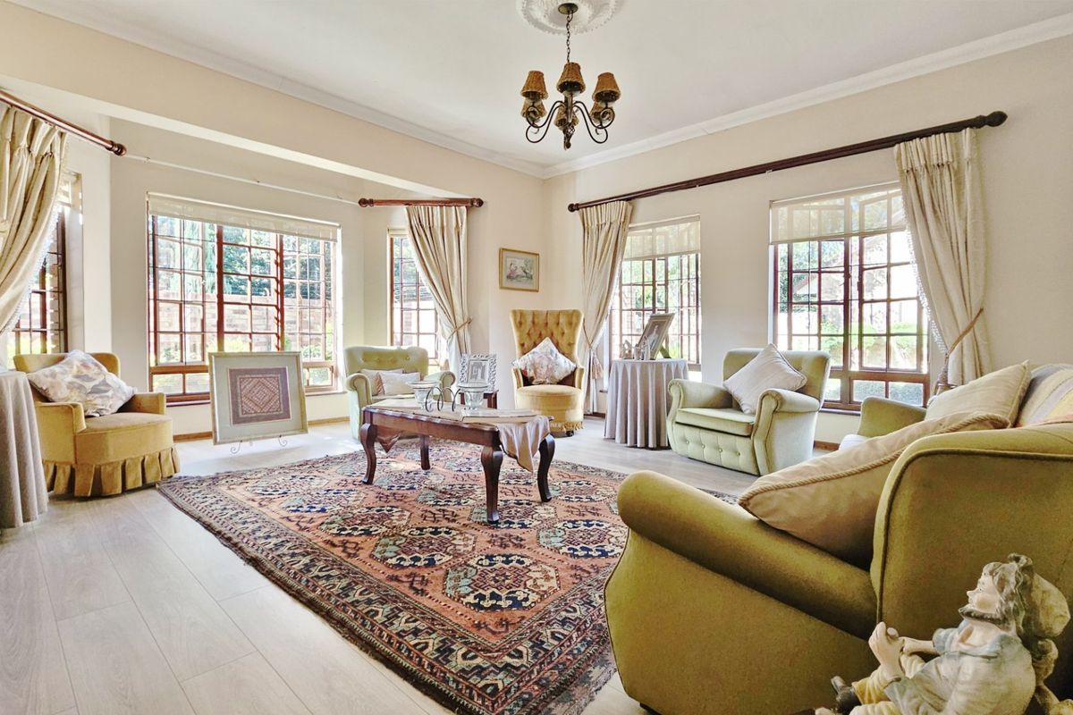 A bright and spacious living room featuring laminate flooring, classic ceiling detailing, and large multi-pane windows that provide ample natural light.