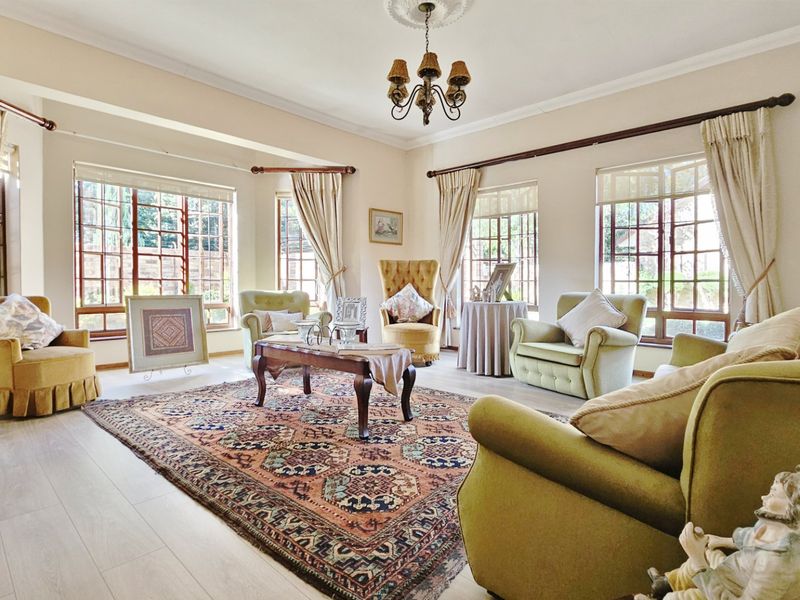 A bright and spacious living room featuring laminate flooring, classic ceiling detailing, and large multi-pane windows that provide ample natural light.