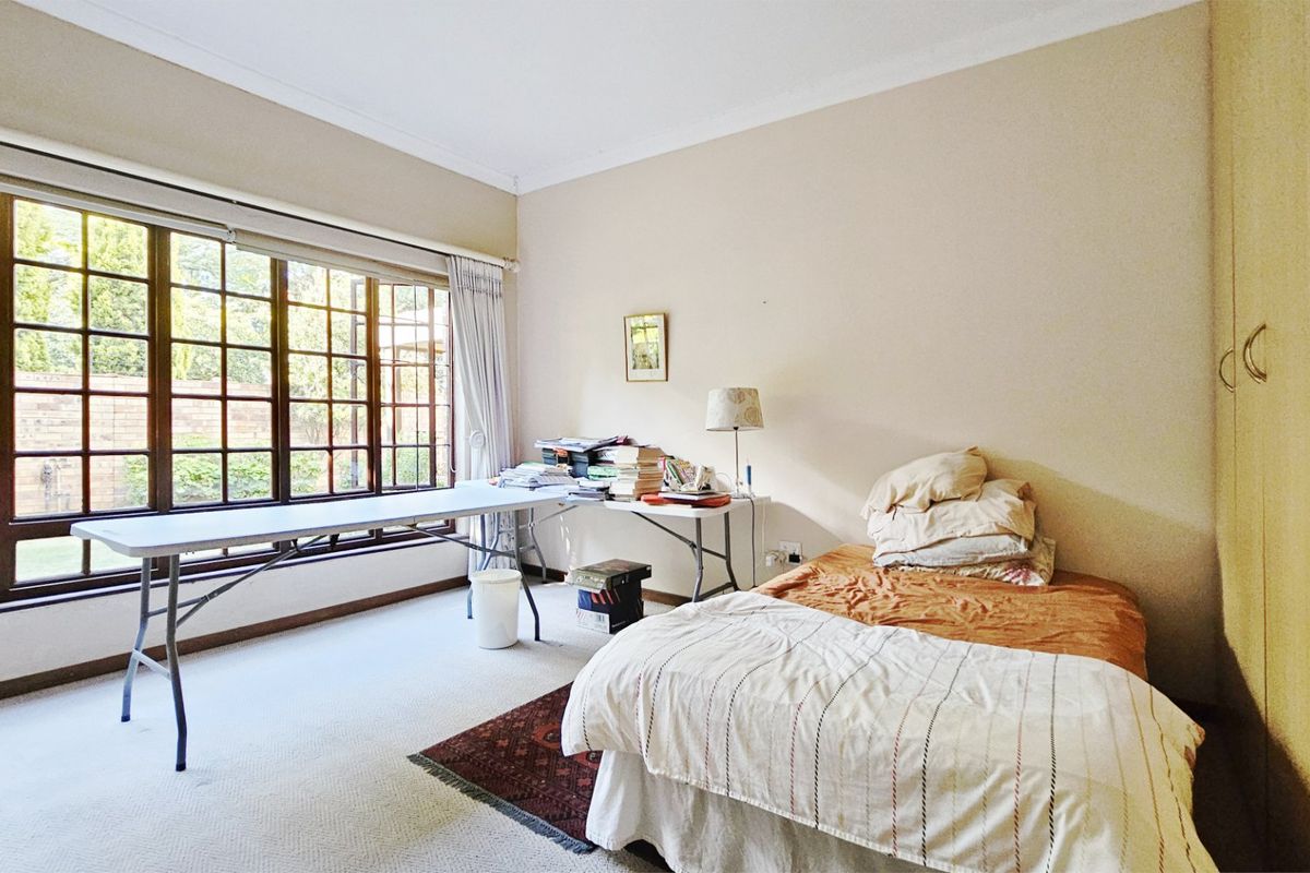 A bedroom featuring built-in cupboards and a large timber-framed window providing natural light and garden views.
