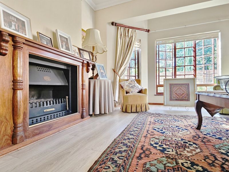 A cozy living room featuring a classic wooden fireplace mantel, laminate flooring, and large windows that provide ample natural light.