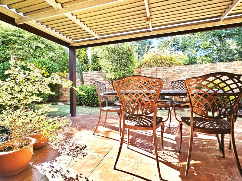 A covered outdoor patio area featuring tiled flooring and a brick boundary wall, overlooking a private garden space.