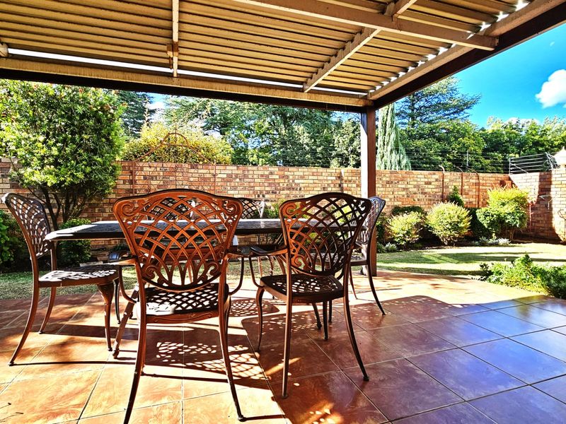 A covered outdoor patio featuring tiled flooring and a brick boundary wall with electric fencing, overlooking a private garden area.