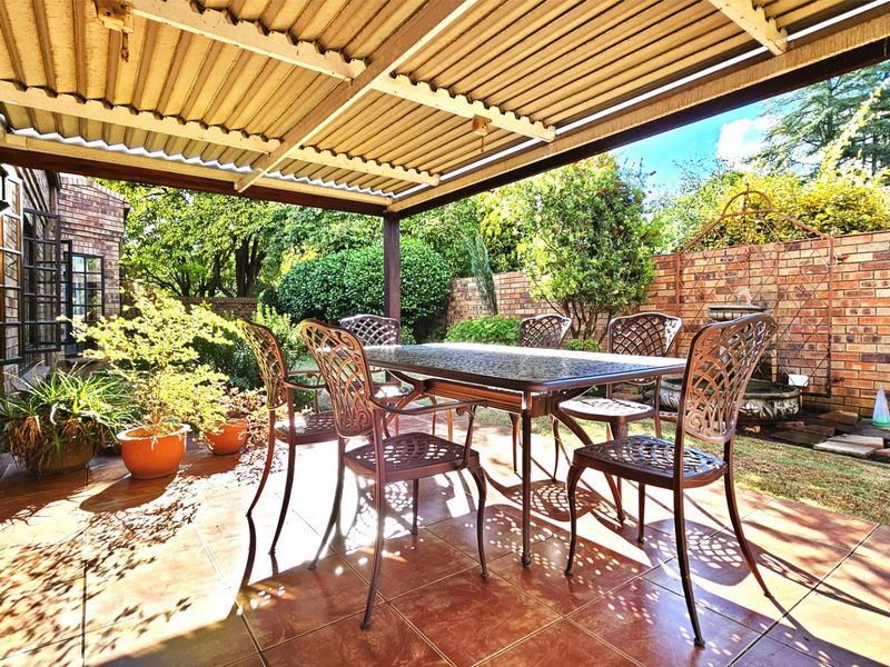 Covered outdoor patio featuring tiled flooring and a corrugated metal roof, providing a sheltered space overlooking the rear garden and brick boundary wall.
