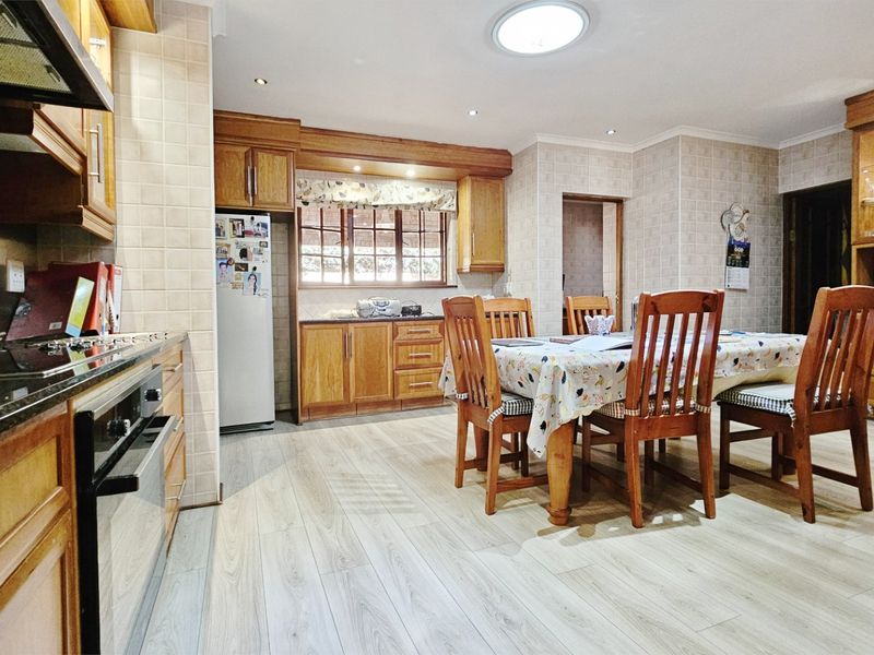 Open-plan kitchen and dining area featuring traditional wooden cabinetry, laminate flooring, and integrated appliances, offering a functional and warm living space.