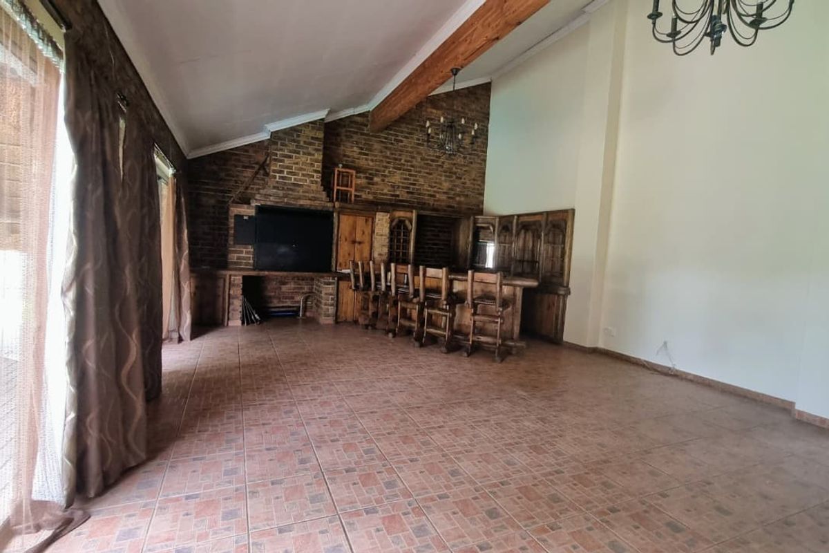 Spacious living area featuring a vaulted ceiling with exposed timber beams, tiled flooring, a built-in brick fireplace, and a custom wooden bar counter.
