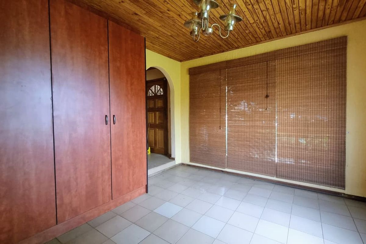 An empty bedroom featuring a built-in wardrobe, tiled flooring, and a timber-paneled ceiling, offering a blank canvas for renovation.