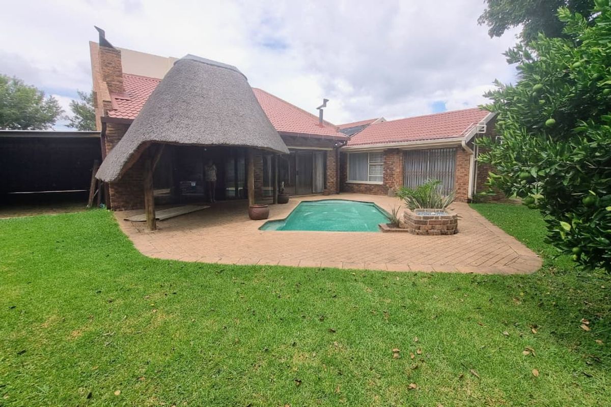 Rear exterior view featuring a swimming pool, paved patio area, and a traditional thatched roof structure attached to the main house.