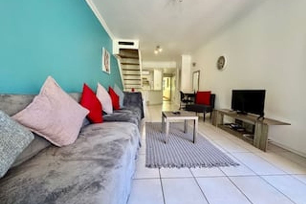 A living room featuring tiled flooring and an internal staircase, leading towards the kitchen area.