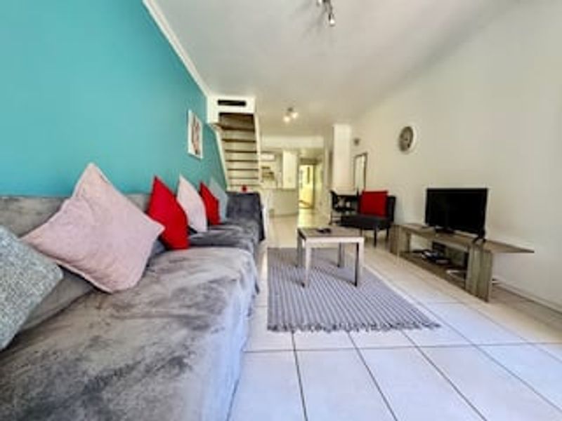 A living room featuring tiled flooring and an internal staircase, leading towards the kitchen area.