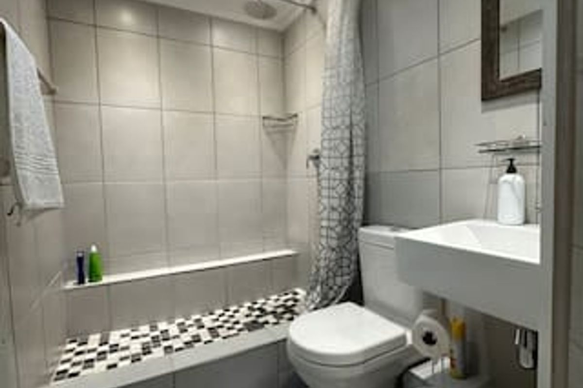 A compact, modern bathroom featuring a tiled shower area, wall-mounted basin, and toilet with neutral grey wall tiles.