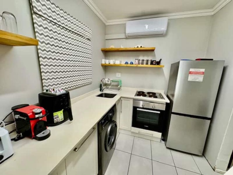 Compact kitchen featuring built-in oven, electric hob, undermount sink, floating timber shelving, and a wall-mounted air conditioning unit.