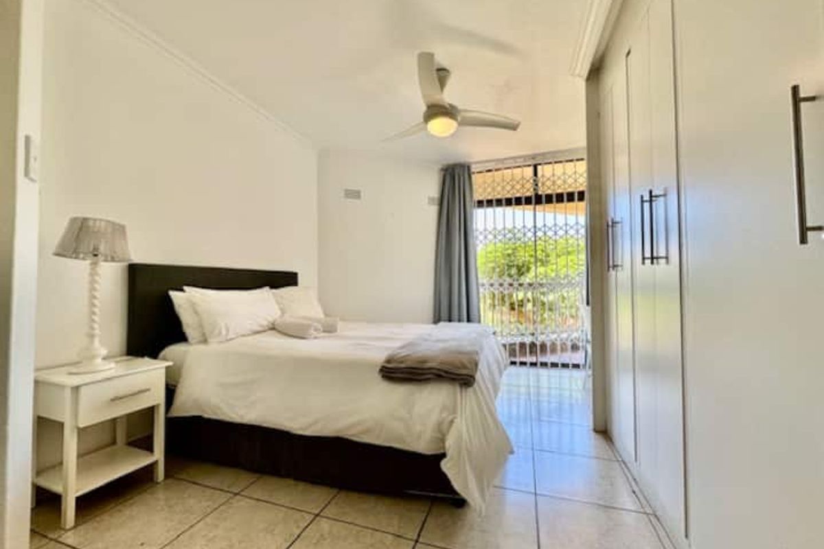 A bright bedroom featuring built-in cupboards, tiled flooring, a ceiling fan, and a security gate leading to an outdoor area.