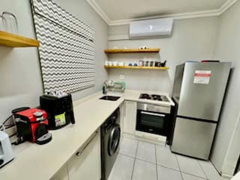 A compact, modern kitchen featuring built-in cabinetry, integrated appliances, a stainless steel sink, and wall-mounted air conditioning, finished with clean tiled flooring.