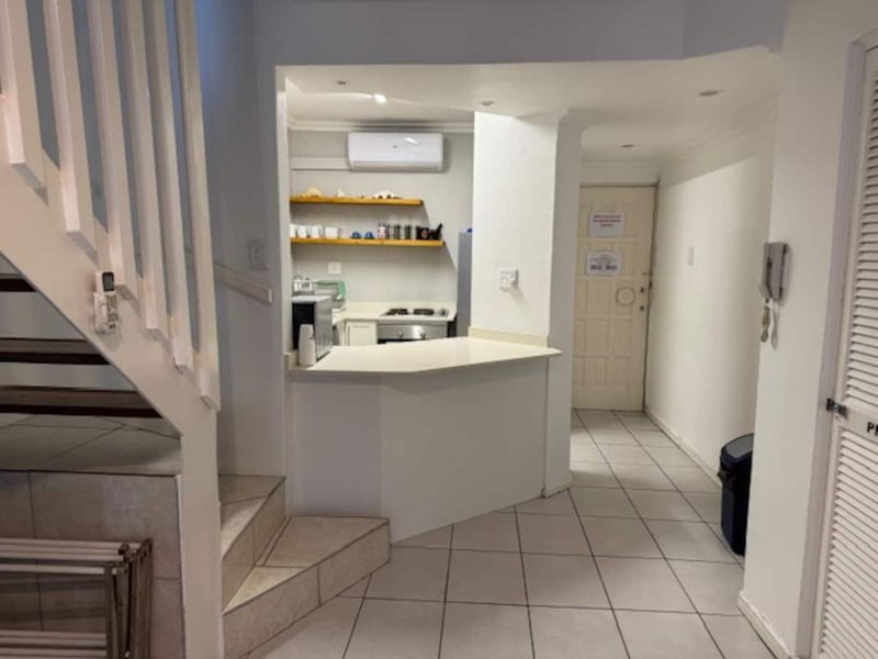 Open plan living area featuring a breakfast bar, built-in shelving, tiled flooring, and a staircase leading to the upper level.