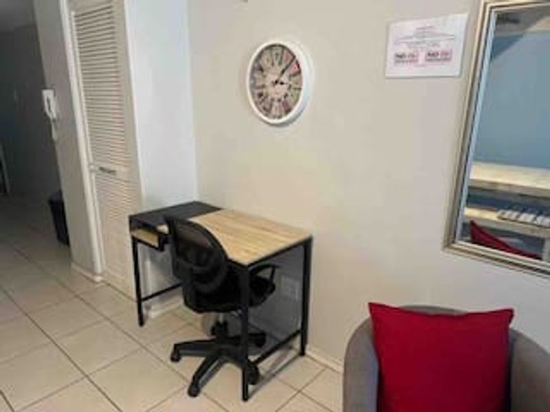A functional hallway area featuring tiled flooring and a louvered closet door, currently utilized as a small workspace.