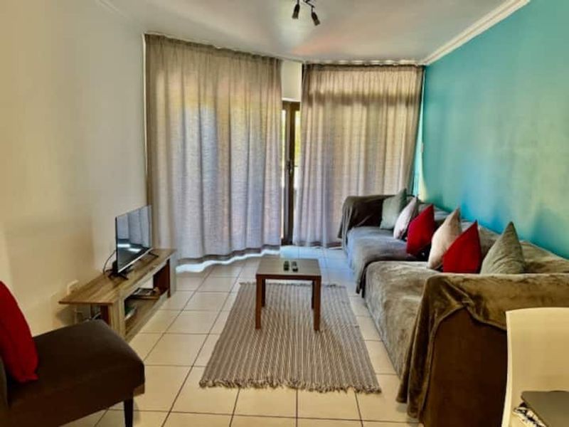 A comfortable living room featuring ceramic floor tiles, track lighting, and large sliding glass doors that provide access to the outdoor area.